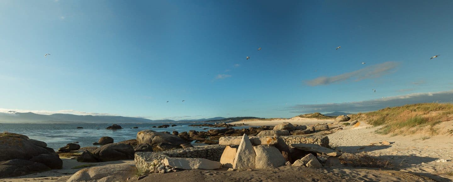 Restos megalíticos y rocas de granito en una playa del Islote de Areoso con gaviotas al atardecer, Ría de Arousa